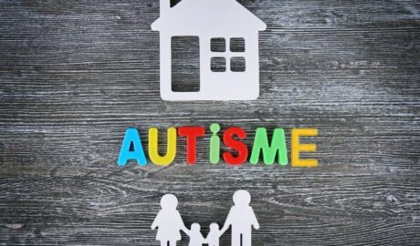 Sur une ardoise, des objets en plastique : une maison, dessous les lettres formant le mot "autisme" et encore dessus des silhouettes d'une famille : la maman et le papa encadrant 2 enfats et les tenant par la main