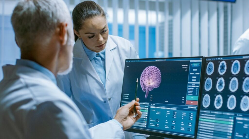 Recherche sur le cerveau - un chercheur assis devant un écran d'ordinateur avec des images de cerveaux et une chercheuse debout qui regarde les images