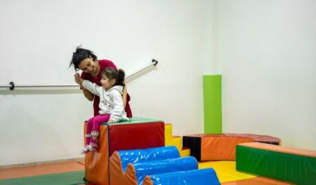 Une petite fille aidée par une dame sur du matériel de gym (escaliers en plastique sur du revêtement de sol de gym)